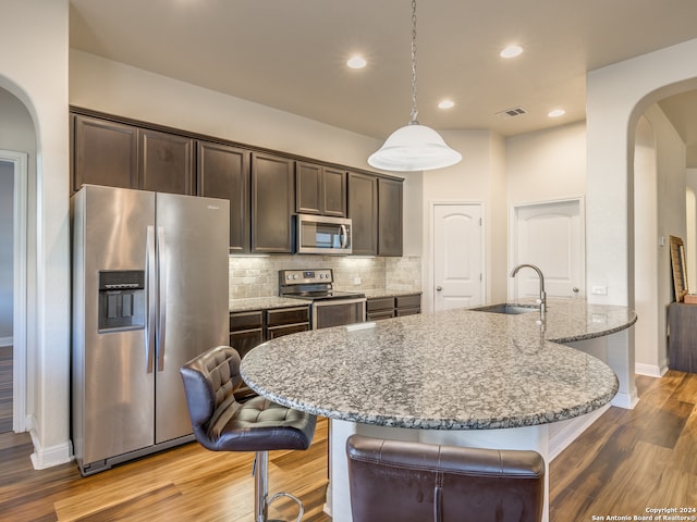 kitchen with sink, light stone counters, decorative light fixtures, appliances with stainless steel finishes, and light wood-type flooring