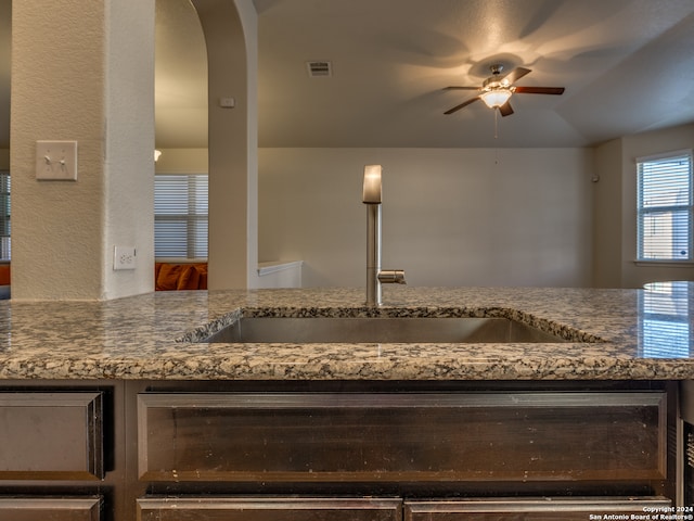 kitchen featuring lofted ceiling, ceiling fan, sink, and stone countertops