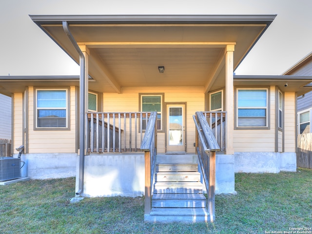 view of exterior entry featuring central AC unit and a lawn