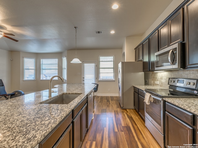 kitchen featuring sink, dark hardwood / wood-style floors, dark stone countertops, decorative light fixtures, and stainless steel appliances