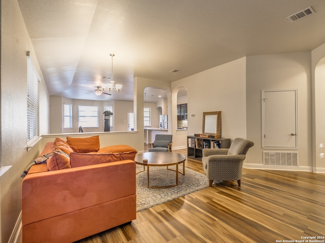 living room with a textured ceiling, ceiling fan with notable chandelier, hardwood / wood-style flooring, and vaulted ceiling