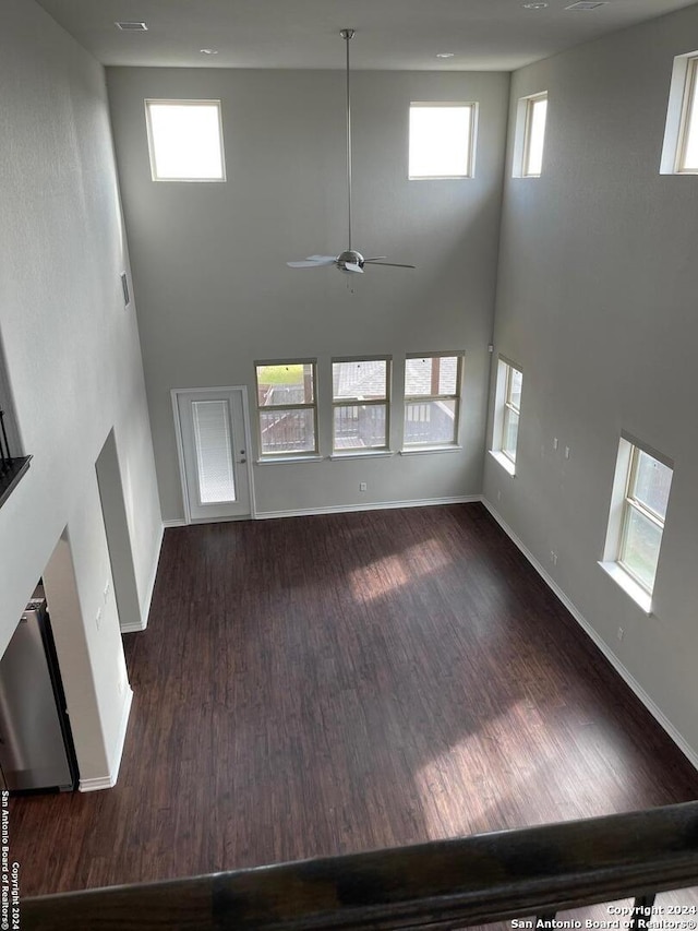 unfurnished living room featuring ceiling fan, dark hardwood / wood-style flooring, a towering ceiling, and a wealth of natural light