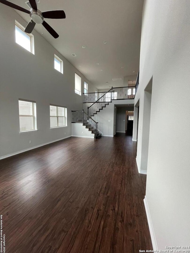 unfurnished living room with a towering ceiling, plenty of natural light, dark wood-type flooring, and ceiling fan