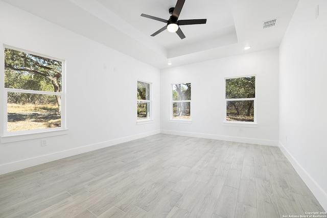 spare room featuring a raised ceiling, a wealth of natural light, ceiling fan, and light wood-type flooring