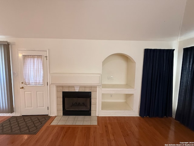 unfurnished living room with built in shelves, a tiled fireplace, and wood-type flooring