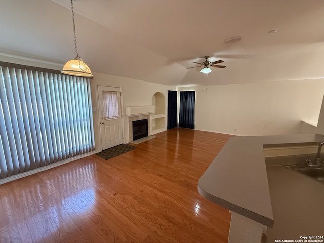 unfurnished living room with ceiling fan, sink, wood-type flooring, lofted ceiling, and a tiled fireplace