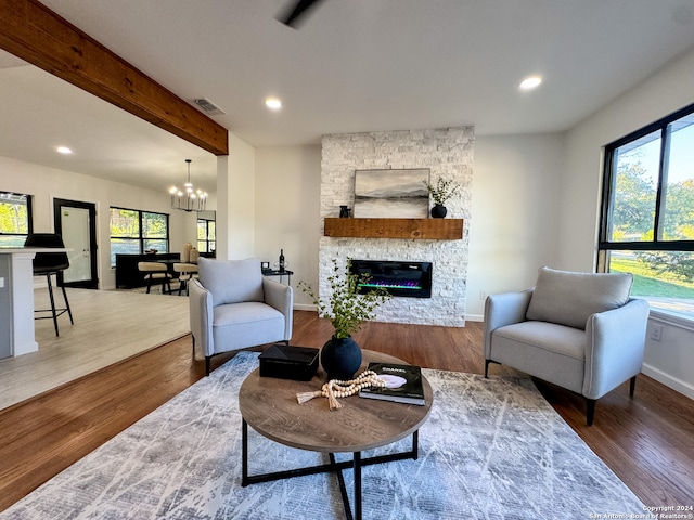 living room with a fireplace, wood-type flooring, a notable chandelier, and beam ceiling