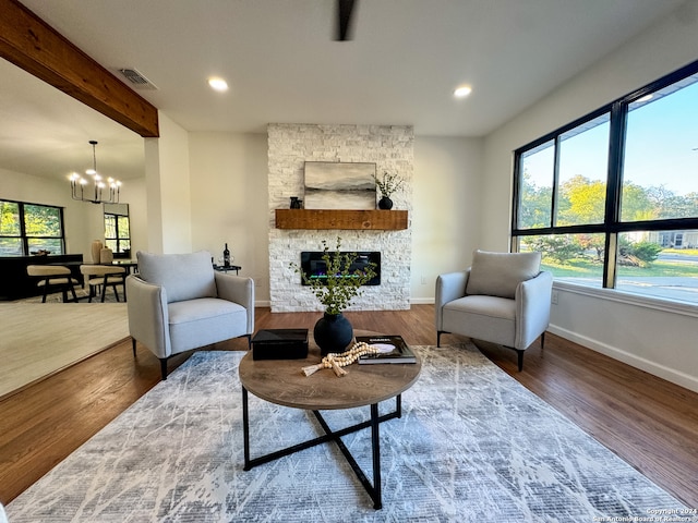 living room featuring a fireplace, hardwood / wood-style floors, beamed ceiling, and a notable chandelier