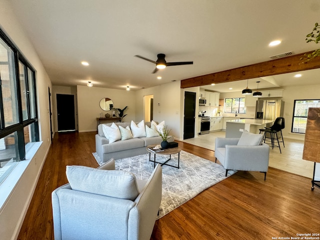 living room featuring ceiling fan, beam ceiling, and light wood-type flooring