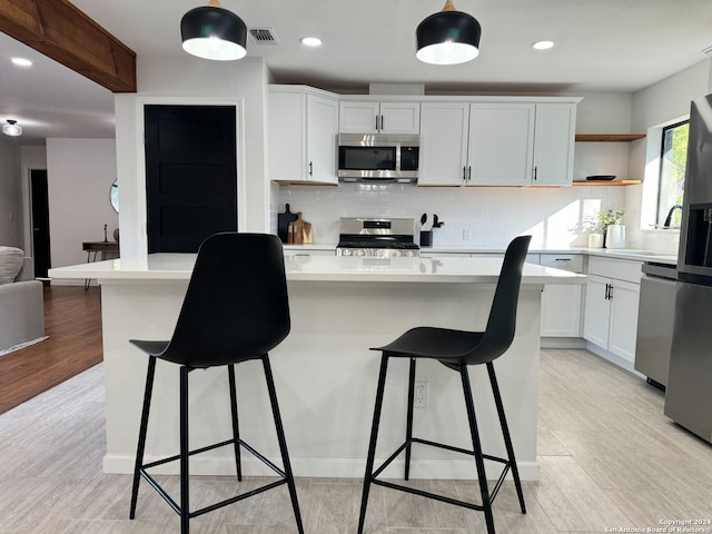 kitchen with stainless steel appliances, a kitchen bar, decorative backsplash, white cabinets, and light wood-type flooring