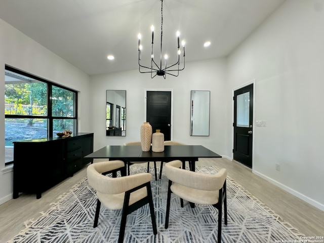 dining room featuring light hardwood / wood-style flooring, a healthy amount of sunlight, vaulted ceiling, and an inviting chandelier