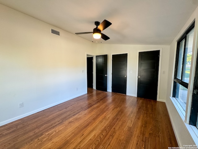 unfurnished bedroom with wood-type flooring, two closets, ceiling fan, and lofted ceiling