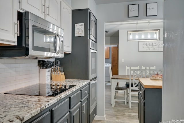 kitchen featuring light wood-type flooring, black electric cooktop, light stone counters, white cabinetry, and washer / clothes dryer