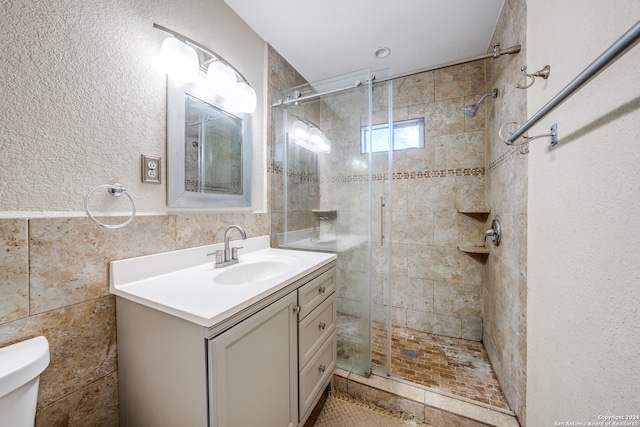 bathroom featuring walk in shower, vanity, tile walls, and toilet