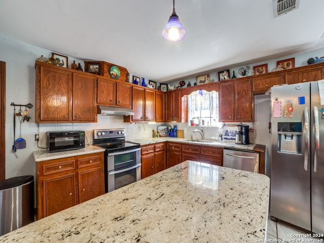 kitchen with sink, tasteful backsplash, decorative light fixtures, light stone counters, and stainless steel appliances