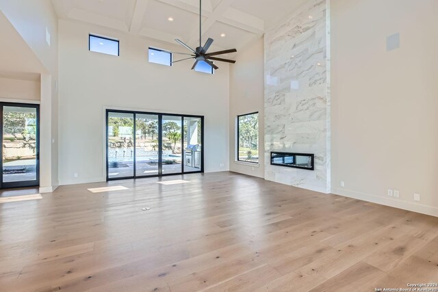 unfurnished living room with ceiling fan, a high ceiling, a premium fireplace, beamed ceiling, and light hardwood / wood-style floors