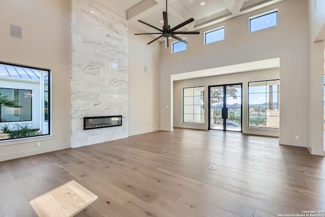 unfurnished living room with a high end fireplace, light wood-type flooring, coffered ceiling, ceiling fan, and beamed ceiling