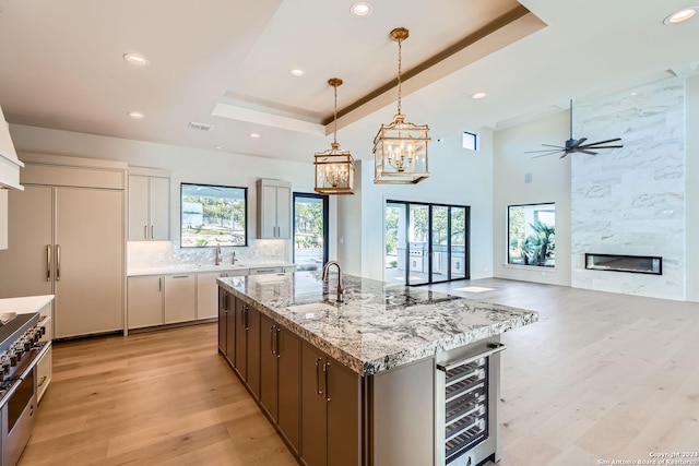 kitchen featuring a tray ceiling, beverage cooler, sink, pendant lighting, and a center island with sink