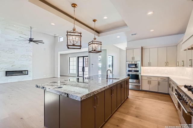 kitchen with sink, hanging light fixtures, stainless steel appliances, a raised ceiling, and light stone counters