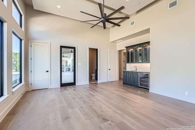 unfurnished living room with beam ceiling, a towering ceiling, light hardwood / wood-style flooring, and wine cooler