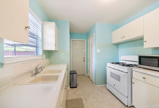 kitchen with light tile patterned floors, white cabinetry, white gas stove, and sink