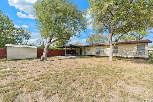 rear view of property featuring a carport, a storage unit, cooling unit, and a lawn