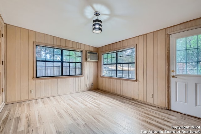 spare room with light wood-type flooring, wooden walls, a wall unit AC, and a healthy amount of sunlight