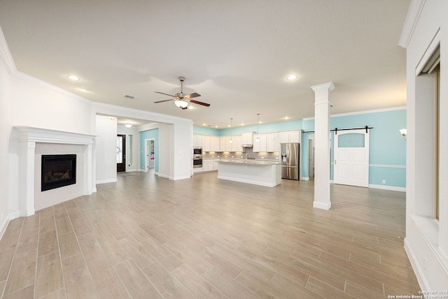 unfurnished living room with a barn door, ceiling fan, light hardwood / wood-style floors, and ornamental molding