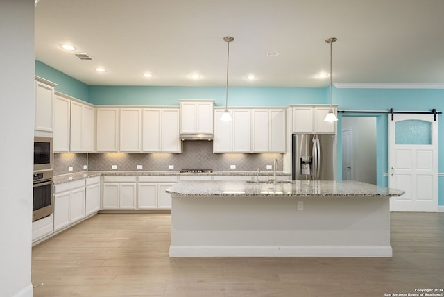 kitchen featuring a barn door, a center island with sink, stainless steel appliances, and decorative light fixtures