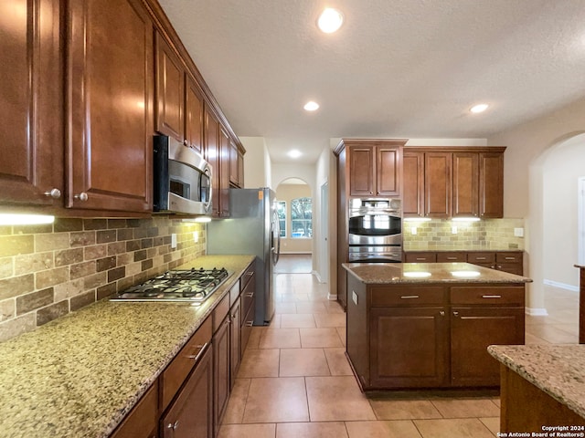 kitchen featuring decorative backsplash, appliances with stainless steel finishes, light stone counters, and light tile patterned flooring