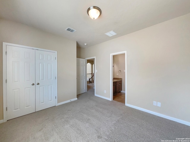 unfurnished bedroom with ensuite bathroom, light colored carpet, and a closet