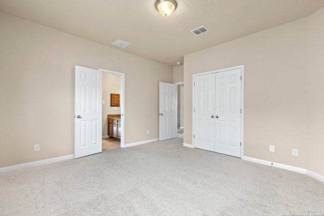 unfurnished bedroom with light carpet, ensuite bath, and a closet