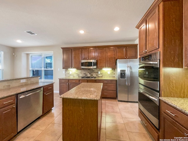 kitchen with decorative backsplash, light stone countertops, a kitchen island, and appliances with stainless steel finishes