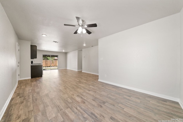 unfurnished living room featuring ceiling fan, light wood-type flooring, and a textured ceiling