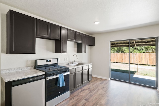 kitchen featuring dark brown cabinetry, sink, stainless steel appliances, a textured ceiling, and light wood-type flooring