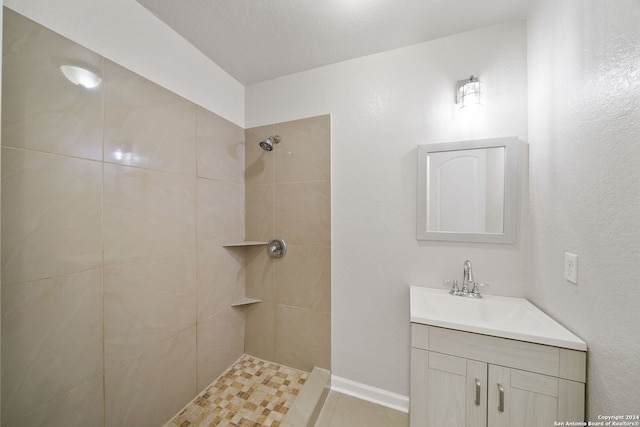 bathroom with tile patterned flooring, vanity, a tile shower, and a textured ceiling