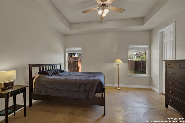 bedroom with a raised ceiling, multiple windows, and ceiling fan