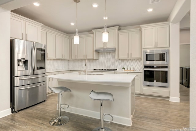 kitchen featuring pendant lighting, stainless steel appliances, light hardwood / wood-style flooring, and a center island with sink