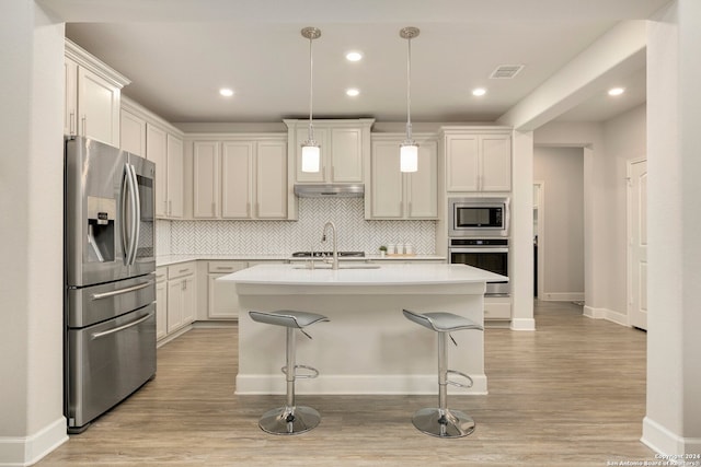 kitchen with hanging light fixtures, light hardwood / wood-style flooring, a kitchen bar, a center island with sink, and appliances with stainless steel finishes