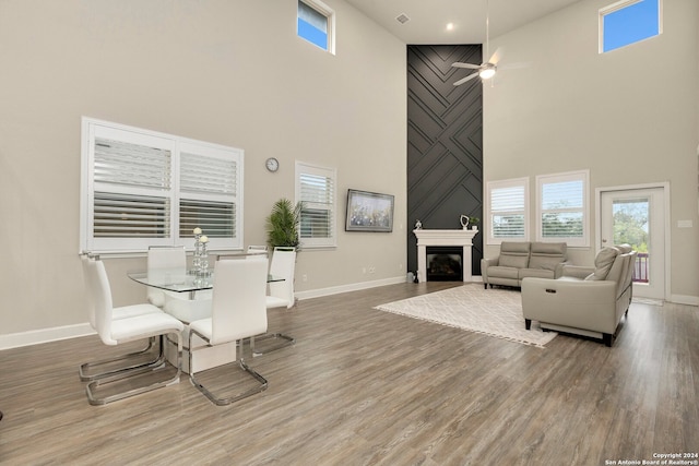 dining space with a fireplace, hardwood / wood-style floors, a towering ceiling, and ceiling fan