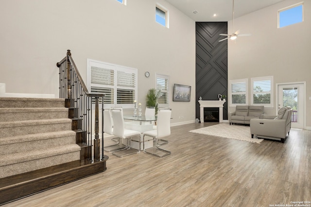 living room with ceiling fan, a large fireplace, a towering ceiling, and hardwood / wood-style floors