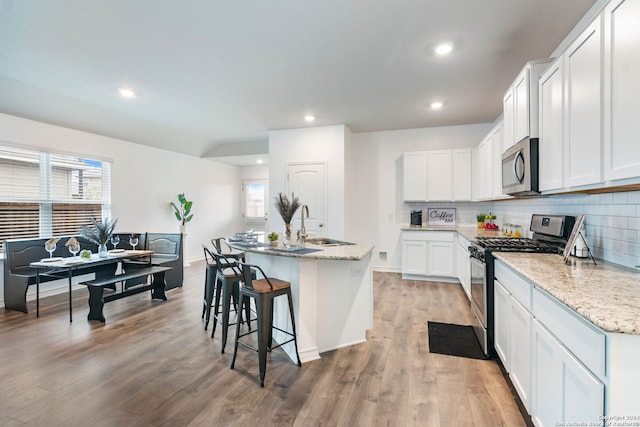 kitchen featuring white cabinetry, stainless steel appliances, plenty of natural light, a center island with sink, and light wood-type flooring