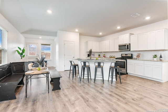 kitchen with backsplash, a kitchen island with sink, light hardwood / wood-style flooring, white cabinetry, and stainless steel appliances