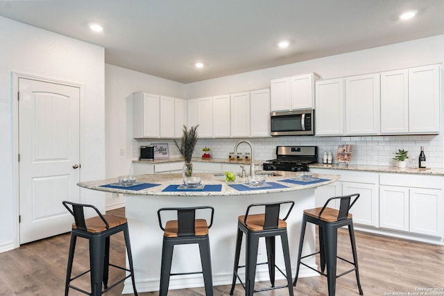 kitchen featuring sink, stainless steel appliances, white cabinetry, and an island with sink