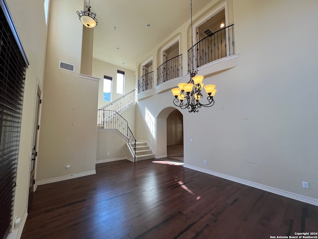 unfurnished living room featuring a towering ceiling, dark hardwood / wood-style floors, and an inviting chandelier