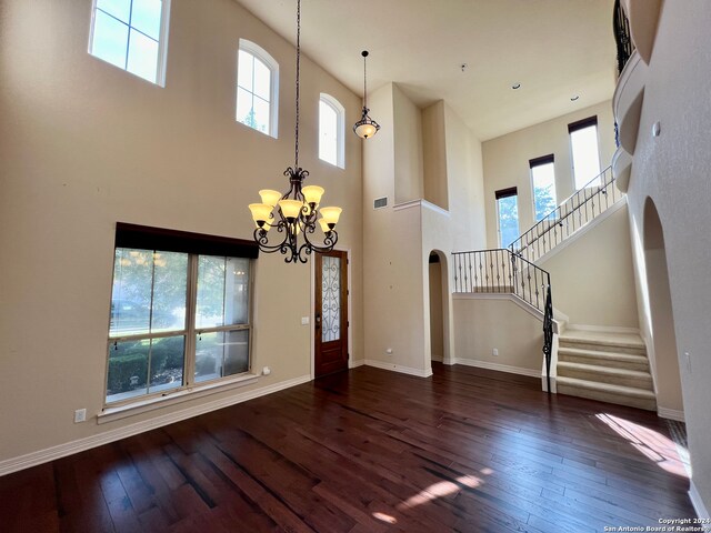 foyer entrance featuring a towering ceiling, dark hardwood / wood-style floors, and a notable chandelier