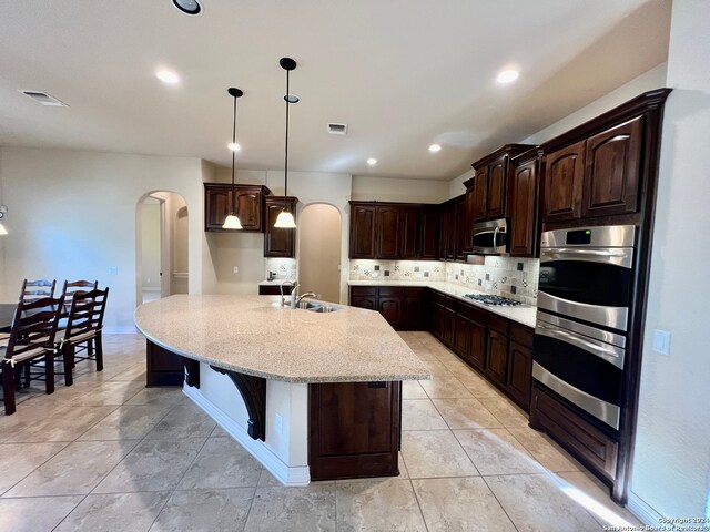 kitchen with backsplash, dark brown cabinets, an island with sink, and appliances with stainless steel finishes