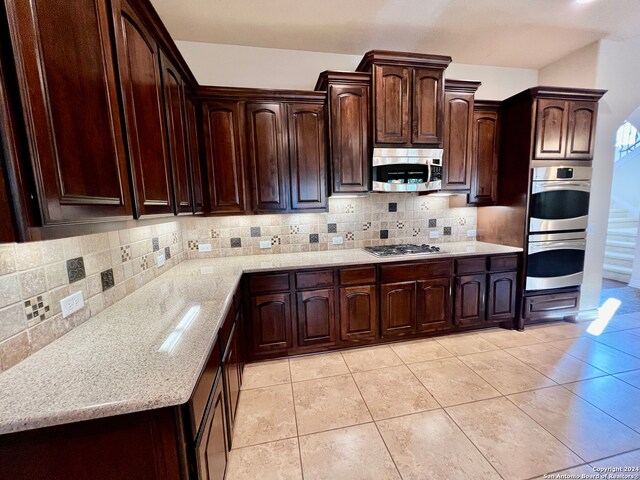 kitchen with decorative backsplash, dark brown cabinets, light tile patterned flooring, light stone counters, and stainless steel appliances