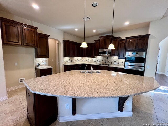 kitchen featuring dark brown cabinetry, stainless steel appliances, a kitchen island with sink, sink, and pendant lighting