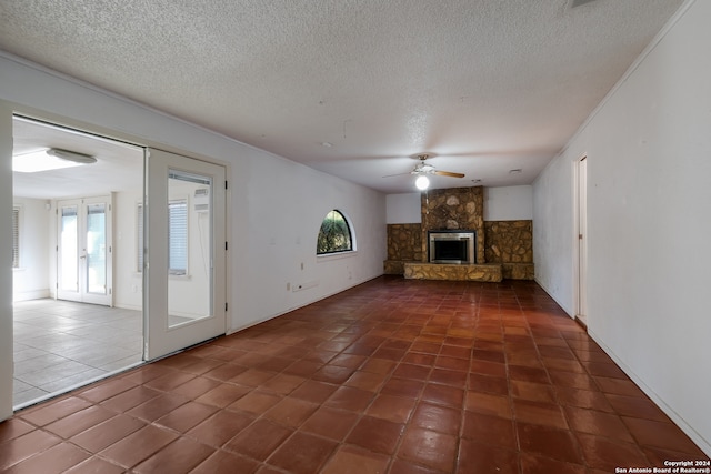 unfurnished living room with a textured ceiling, a stone fireplace, ceiling fan, and dark tile patterned flooring